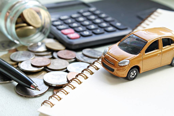 Miniatuur automodel, rekenmachine, munten verspreid uit glazen pot, notebookpapier en pen op kantoor bureau tafel - Foto, afbeelding