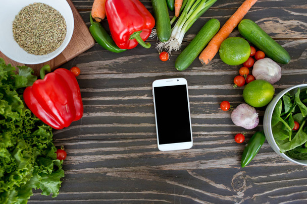 Légumes bio frais et smartphone au centre sur fond bois, concept de livre de recettes numérique et liste d'achats
. - Photo, image