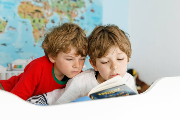 Dos niños pequeños en pijama leyendo un libro en la cama
. - Foto, imagen