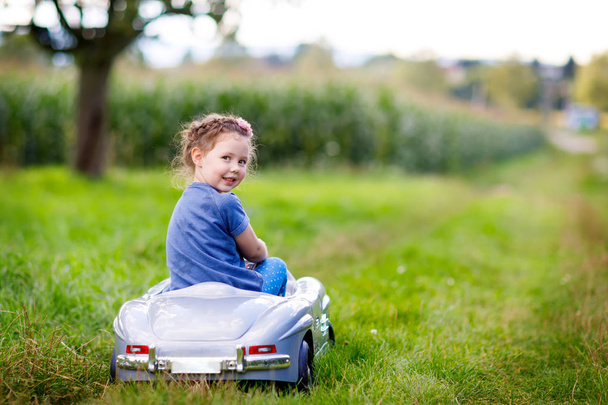 Pequena menina criança pré-escolar sentada no velho carro de brinquedo grande e se divertindo no dia ensolarado de verão
 - Foto, Imagem