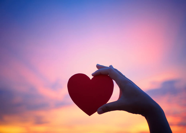 Silhouette main tenant beau coeur pendant le coucher du soleil. Joyeux, Amour, Saint Valentin idée, signe, symbole, concept
. - Photo, image