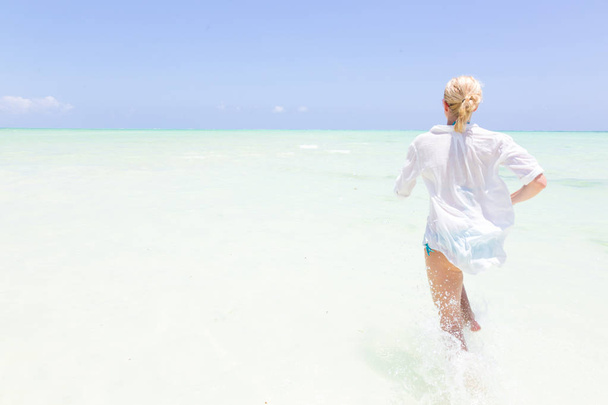 Joven mujer activa divirtiéndose corriendo y salpicando en el agua de mar compañero
. - Foto, Imagen