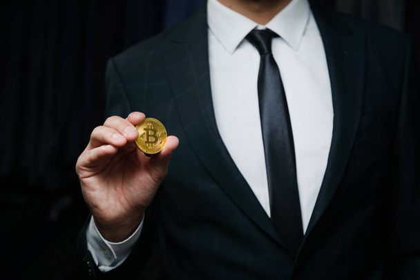 Businessman in a suit holding golden Bitcoin on black background - Фото, изображение