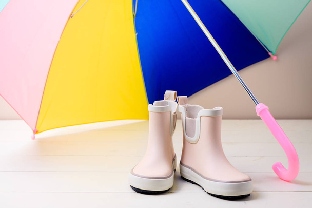 Pinkfarbene kleine Kinder-Gummistiefel stehen unter bunten Regenschirmen - Foto, Bild