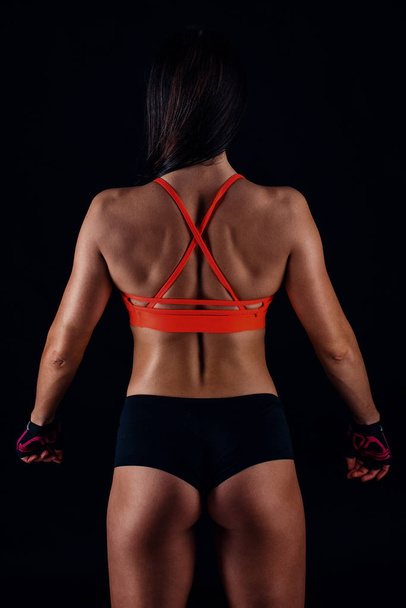 Beautiful fitness sexy slim female in activewear posing over black background. Back view. - 写真・画像