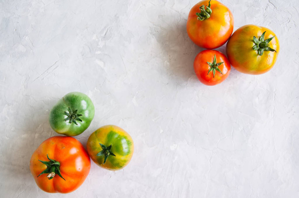 Different sizes of colorful fresh tomatoes on a white stone back - Foto, afbeelding