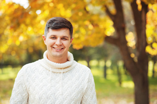 Autumn is coming! Be happy today! Close up portrait of young handsome brunette man staying in autumn park smiling and looking in cam. Emotions, people, season, fashion concepts - Photo, Image