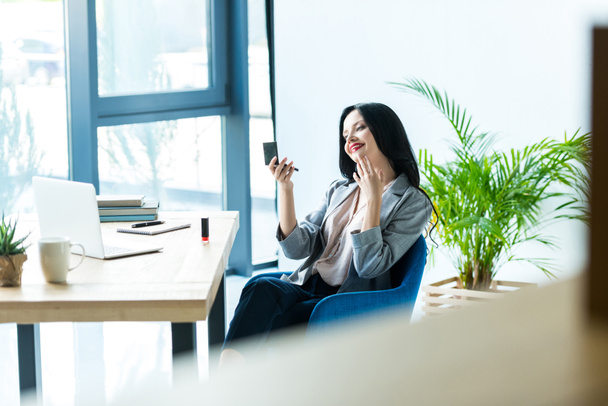 businesswoman applying lipstick at workplace - Fotografie, Obrázek