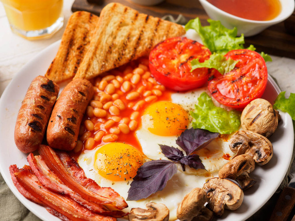 Повний англійський сніданок включає ковбаски, на грилі помідори і гриби, яйце, бекон, Тушкована квасоля, хліб з апельсинового соку - Фото, зображення