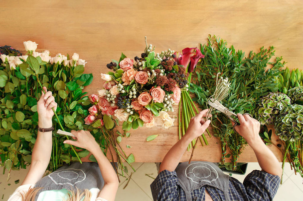 Florist and assistant in flower shop delivery make rose bouquet, table top view - Fotó, kép