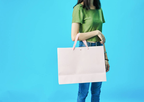 Woman wearing green shirts holding shopping bags in the blue background. - Foto, imagen