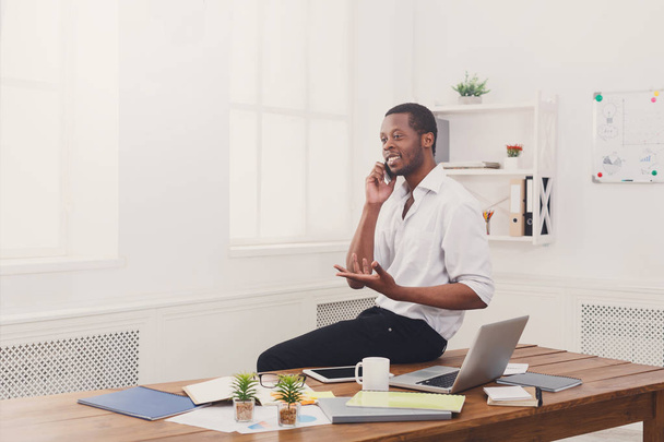 Jonge zwarte zakenman met mobile in moderne witte kantoor - Foto, afbeelding