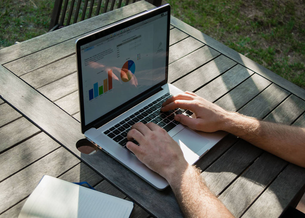 Ręce człowieka za pomocą laptopa z wykresu analitycznego na biurko w pracy w ogrodzie, na świeże powietrze, freelancer - Zdjęcie, obraz