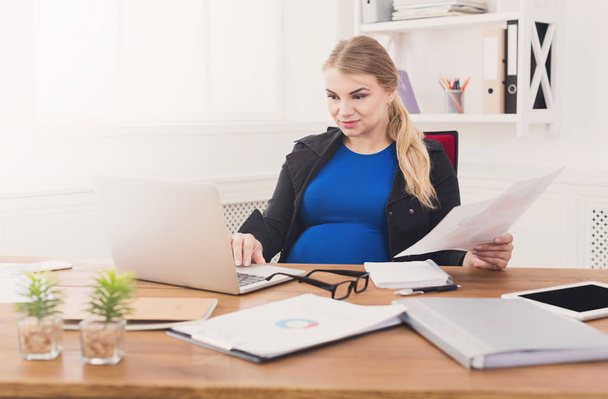 Pregnant business lady at work reading papers - Foto, imagen