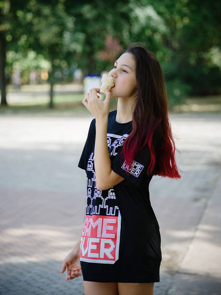 Una encantadora chica hipster de moda en ropa de verano comiendo helado sobre un fondo urbano. Concepto urbano de moda. Copiar espacio
. - Foto, Imagen