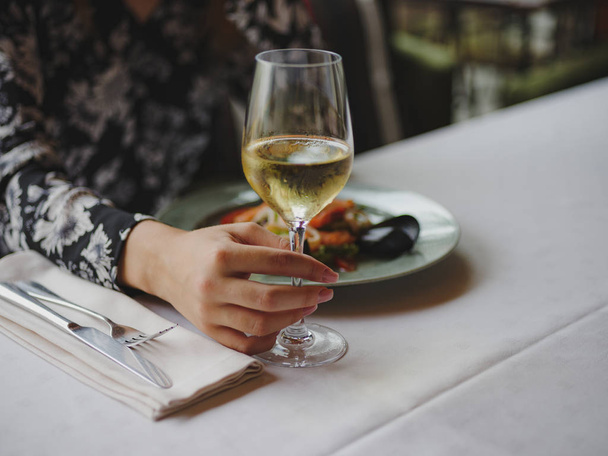 Close-up of a woman at the restaurant. Lady holding wine on a blurred background. Luxurious lunch concept. Copy space. - Fotó, kép
