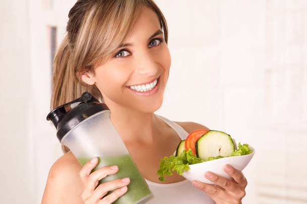 Beautiful young smiling woman wearing a white t-shirt and holding a healthy salad with one hand and therm of juice in her other hand - Foto, imagen