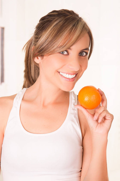 Beautiful young smiling woman wearing a white t-shirt and holding a healthy orange - Photo, image