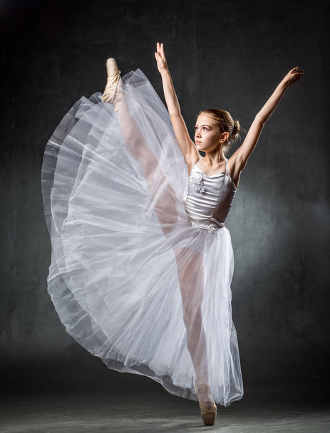 Young girl ballerina showing the dance elements on a dark background. Ballet. - Foto, imagen