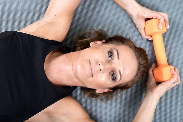 Jeune femme active utilisant un haltère orange pour son exercice du bras dans un studio de fitness fait maison
 - Photo, image