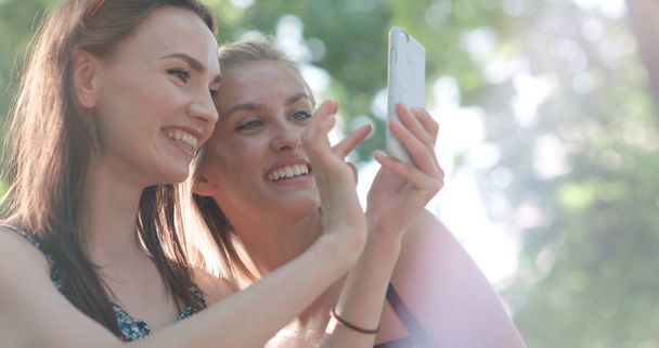 Two beautiful teenage girls using phone in a city park.  - Fotografie, Obrázek