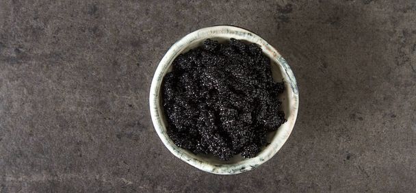 Black sturgeon caviar in a ceramic bowl. Dark background. - Foto, immagini