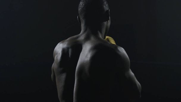 Achteraanzicht van gespierde man Boksen op zwarte achtergrond. Afro Amerikaanse jonge mannelijke bokser beoefenen van schaduw boksen. Boxer in gele bokshandschoenen - Foto, afbeelding