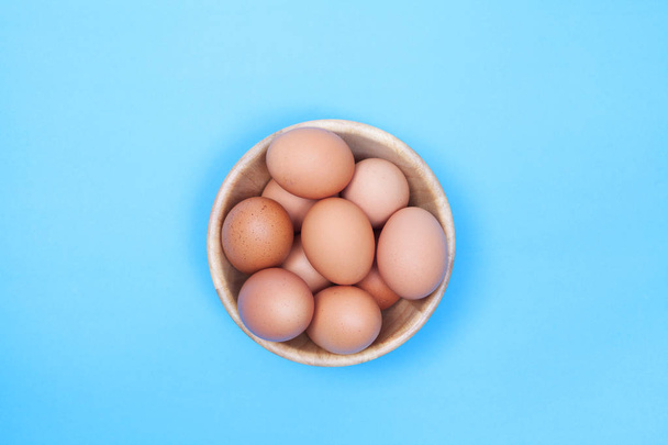 Chicken egg in wood bowl on blue background with space for copy  - Photo, image