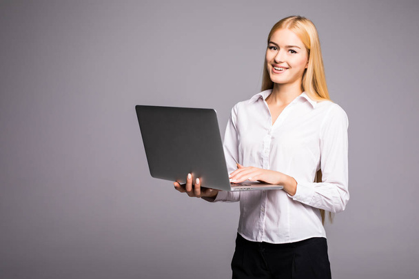 Happy woman holding laptop and looking at camera over gray background - Foto, Imagem