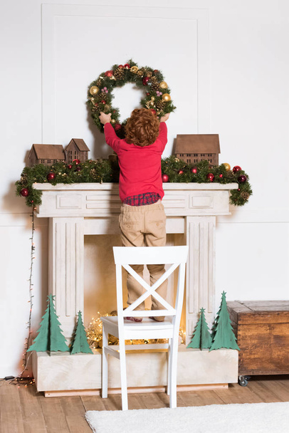 child hanging christmas wreath at home - Fotó, kép