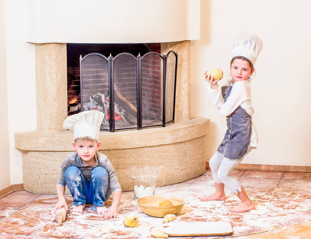 Two siblings - boy and girl - in chef's hats near the fireplace  - Fotó, kép