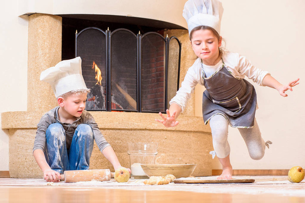 Kaksi sisarusta - poika ja tyttö - keittiömestarin hatuissa takan lähellä  - Valokuva, kuva