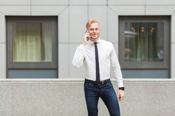 Young adult businessman calling his boss, looking at camera and smiling. - Fotó, kép