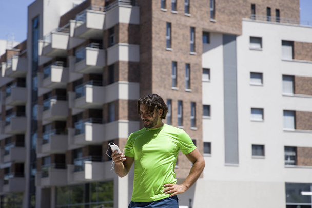 Pohledný mladý muž, používání mobilního telefonu během cvičení - Fotografie, Obrázek
