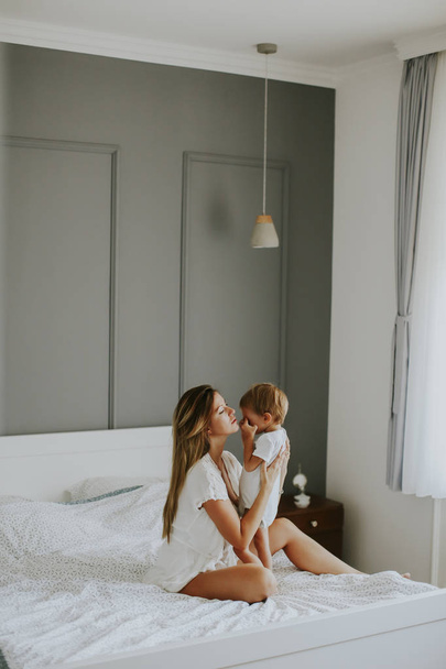 Beyaz yatakta oynayan genç mutlu anne - Fotoğraf, Görsel