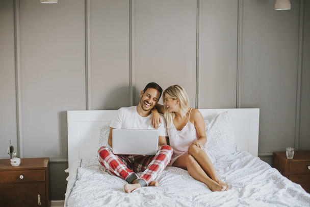 Amoureux intimes en utilisant un ordinateur portable assis sur le lit
 - Photo, image
