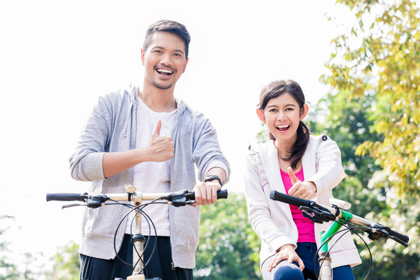 若いアジアのカップル一緒に自転車に乗りながら笑って - 写真・画像