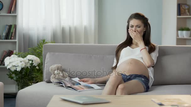 Pregnant lady reading magazine, having light nausea feeling, breathing to relax - Πλάνα, βίντεο