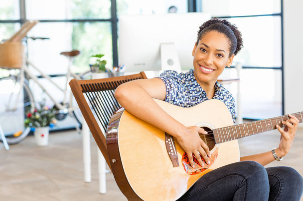 Portrait of smiling afro-american office worker sitting in offfice with guitar - Foto, immagini