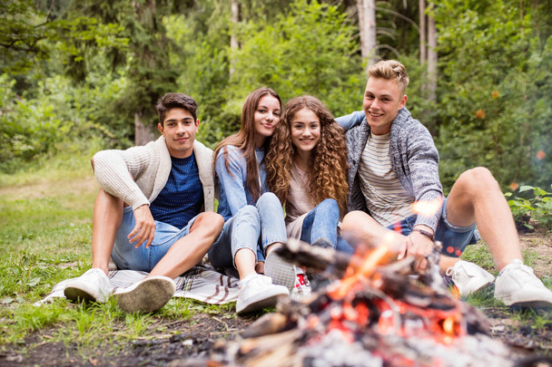 Teenagers camping in nature, sitting at bonfire. - Foto, imagen