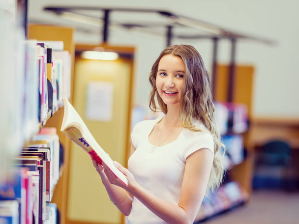 Happy female student picking up books at the library - Фото, зображення