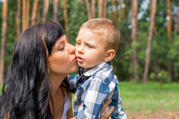 Äiti suutelee hänen pientä poikaansa puistossa aurinkoisena päivänä
 - Valokuva, kuva