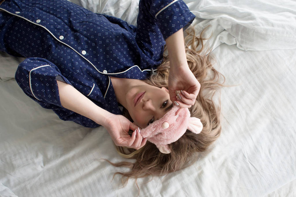 Niedliche Blondine in ihrem Bett im blauen Pyjama und Schlafmaske, Draufsicht - Foto, Bild