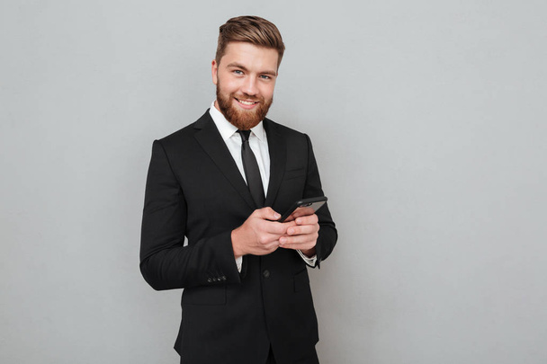 Smiling bearded man in suit using his smartphone - Фото, зображення