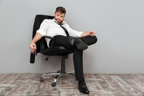 Happy drunk businessman sitting in office chair with bottle - Фото, изображение