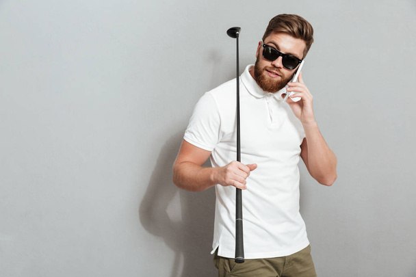 Спокойный гольфист разговаривает со смартфоном и держит клуб
 - Фото, изображение