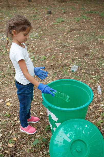 Κάθετη φωτογραφία της childs τα χέρια στο πολύχρωμο ανακύκλωσης σε μπλε γάντια λατέξ. Εξωτερικό φωτογραφία, γης και σκουπιδιών στο φόντο. - Φωτογραφία, εικόνα