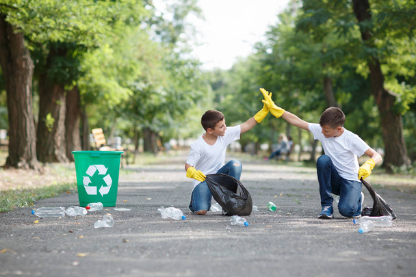 Two cute boys cleaning up the territory and giving each other five on a blurred park background. Ecology protection concept. - Foto, Imagem