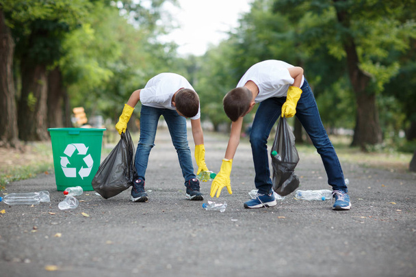 Deux enfants en gants de latex jaune tenant des sacs poubelles noirs et ramassant des ordures sur un fond de parc. Concept d'écologie
. - Photo, image