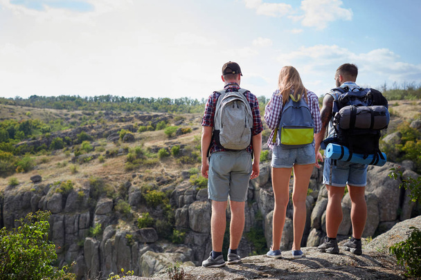 Drie jonge mensen staan op de heuvel. Een bedrijf van vrolijke reizigers op een onscherpe natuurlijke achtergrond. Kopiëren van ruimte. - Foto, afbeelding